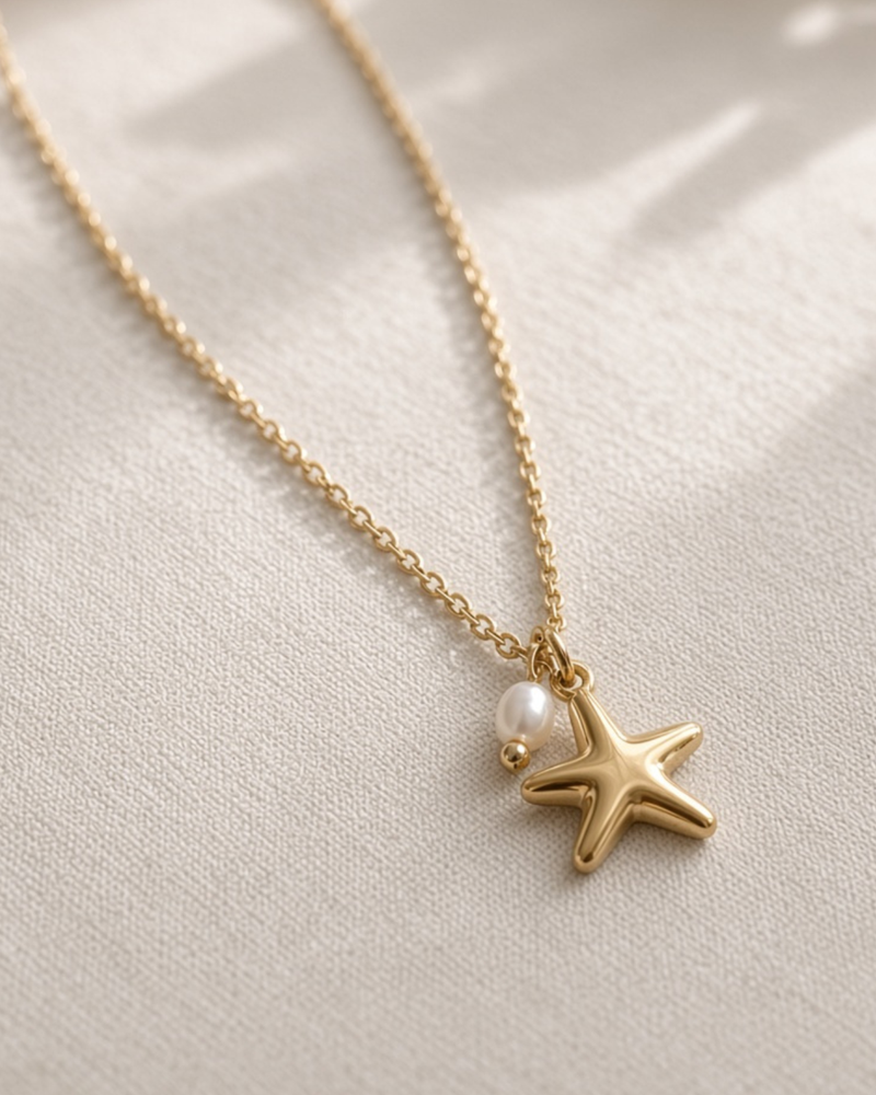 golden starfish necklace with imitation pearl laying on beige linen